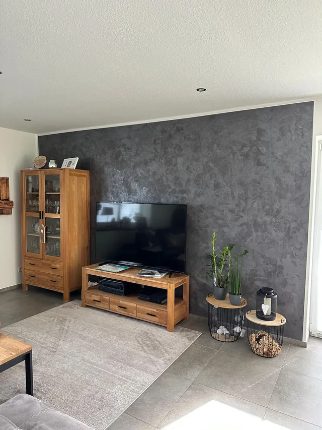 Wohnzimmer mit fugenloser TV-Wand in Spachteltechnik Betonoptik Anthrazit, Eichenmöbel davor – Referenz MB Petersen Malerbetrieb Husum